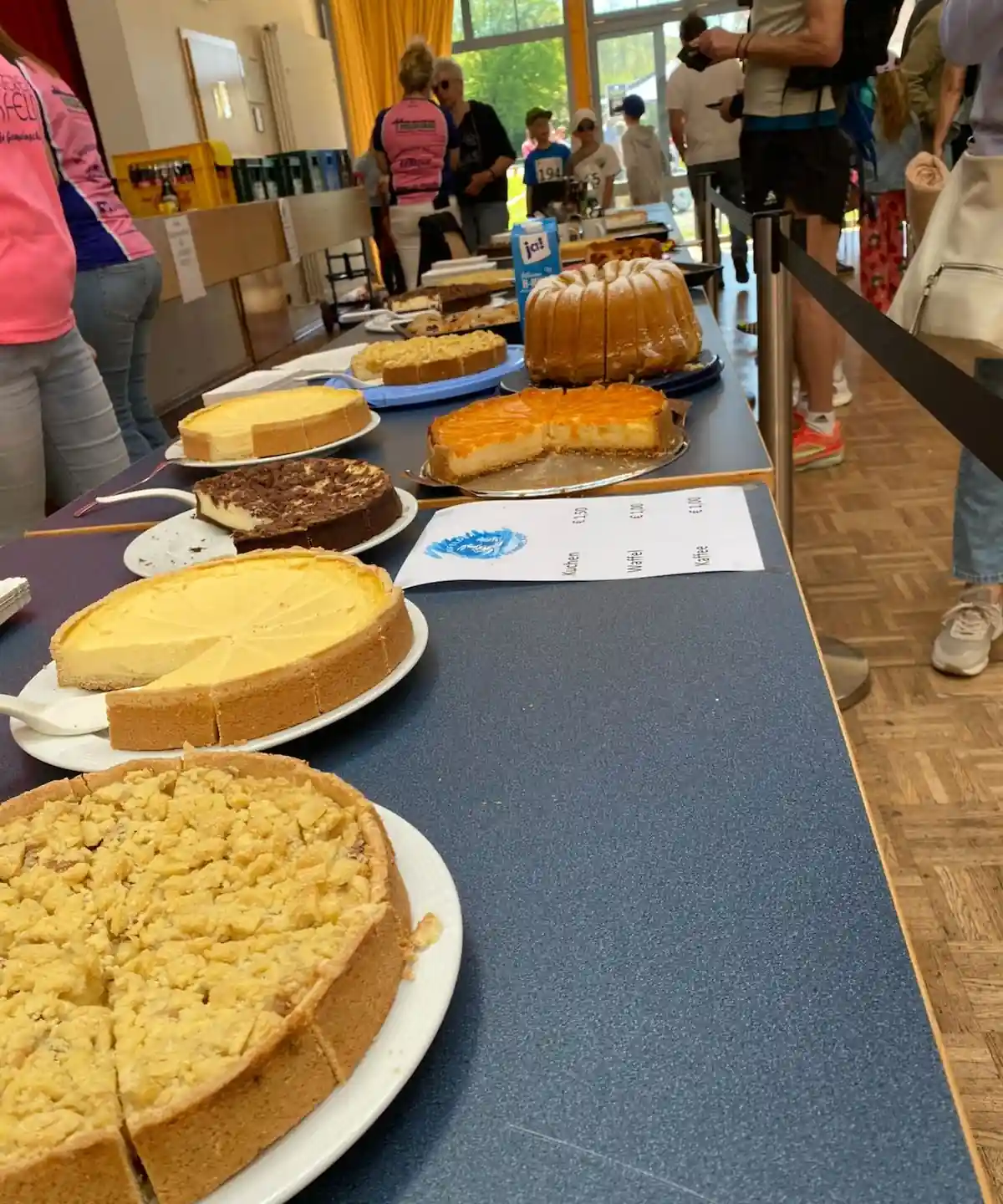 Kuchentheke in der Stadthalle mit Käsekuchen, Streuselkuchen und Napfkuchen, daneben die Preisliste für Kuchen, Waffeln und Kaffee